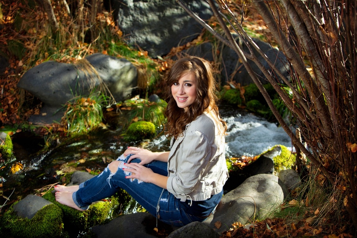 Senior portrait of a student seated on rocks beside a stream
