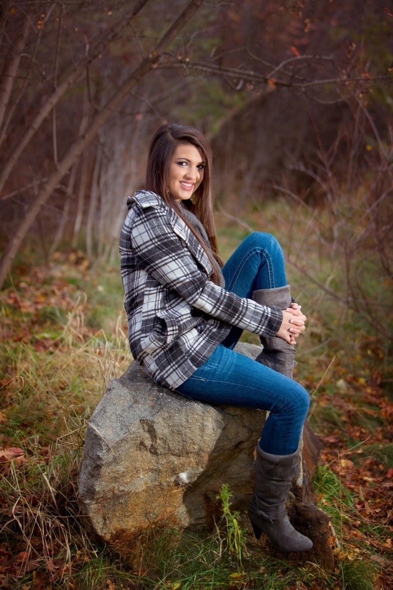 Senior in a plaid shirt and jeans seated in grass