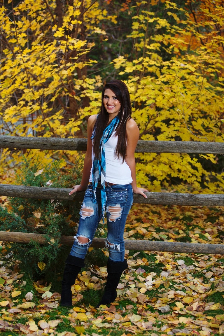 Senior portrait beside a wooden fence with autumn leaves