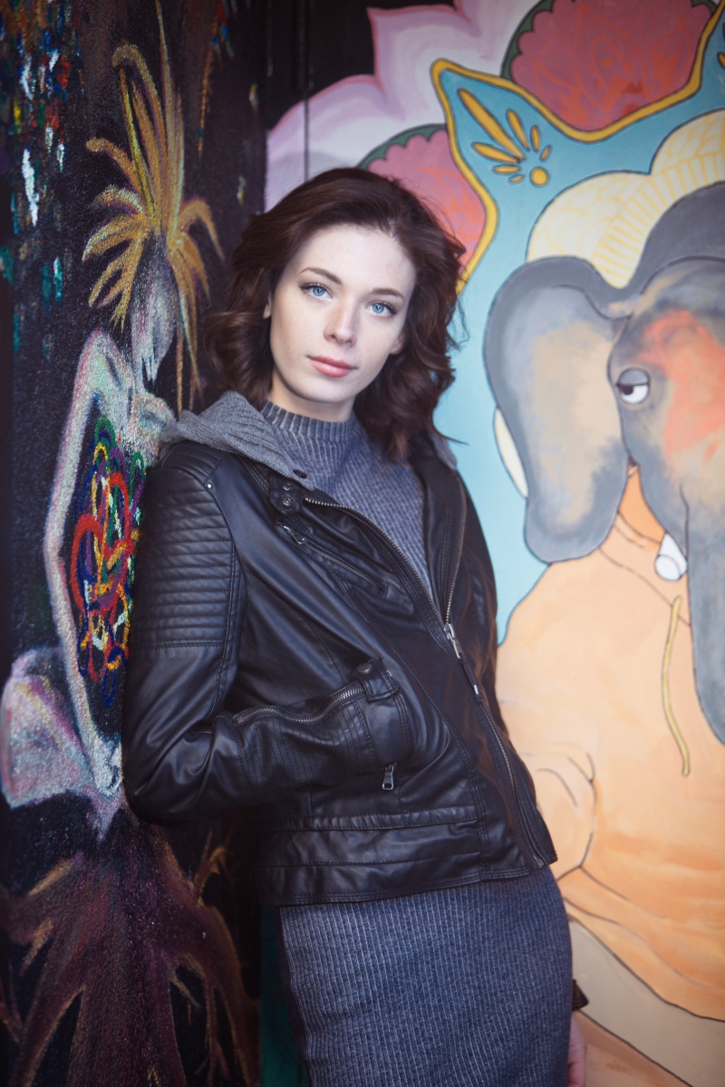 Senior in a dark jacket beside a colorful mural