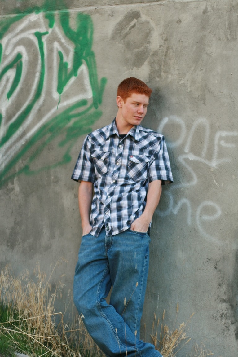Senior in a plaid shirt beside a graffiti-covered wall
