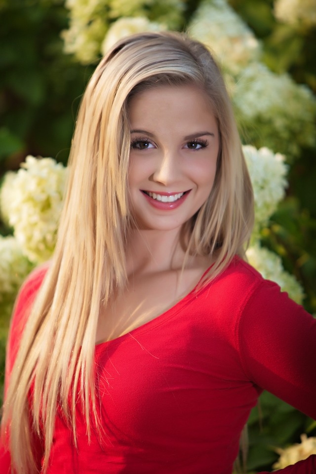 Smiling senior in a red top with a leafy background