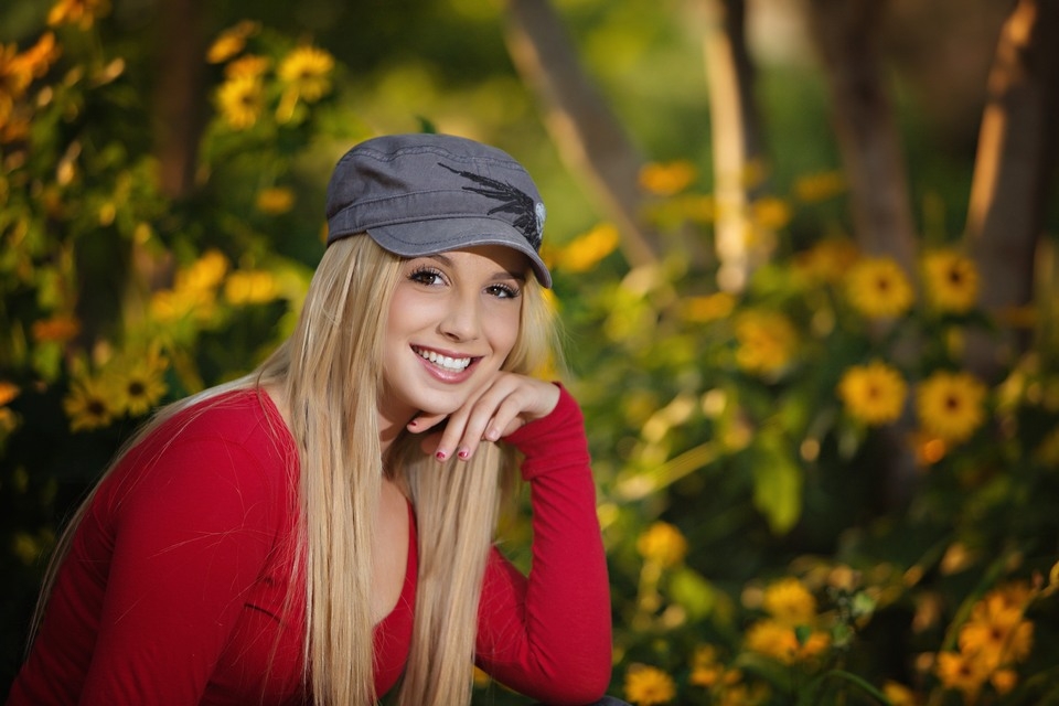 Senior in a cap and red top beside yellow flowers