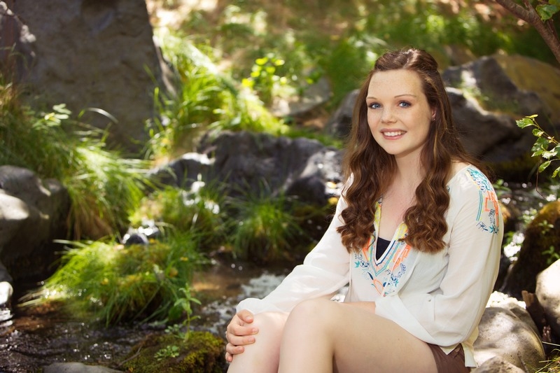 Senior in a white top seated among rocks and greenery