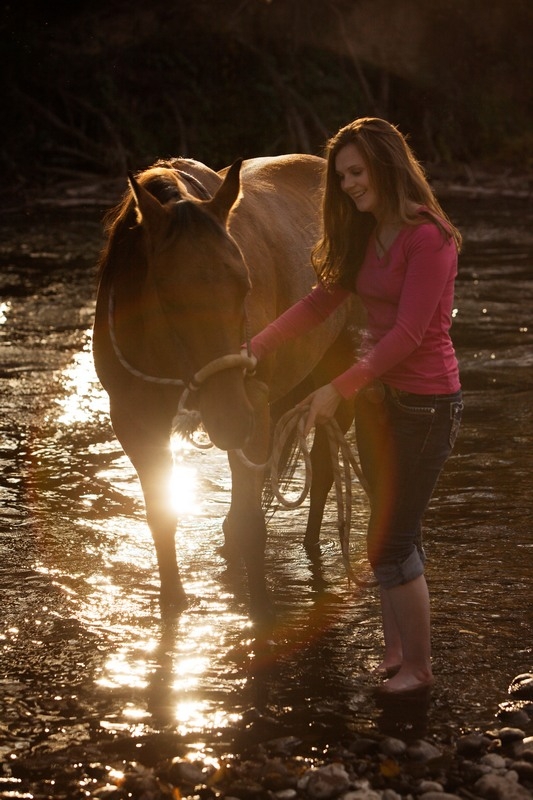 Senior with a horse backlit by sunlight beside water
